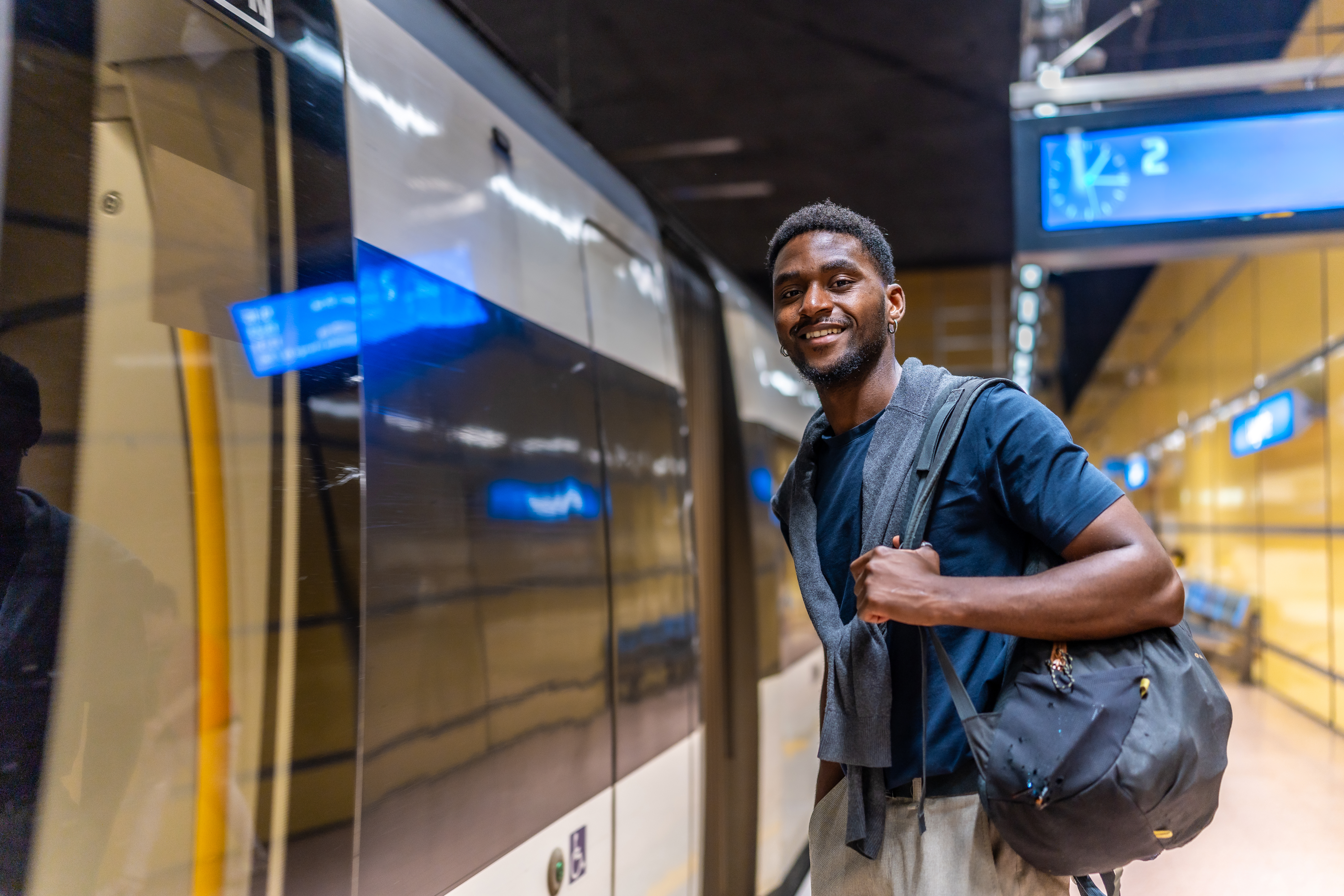 African young businessman waiting for the metro at night standing on the platform and smiling at camera