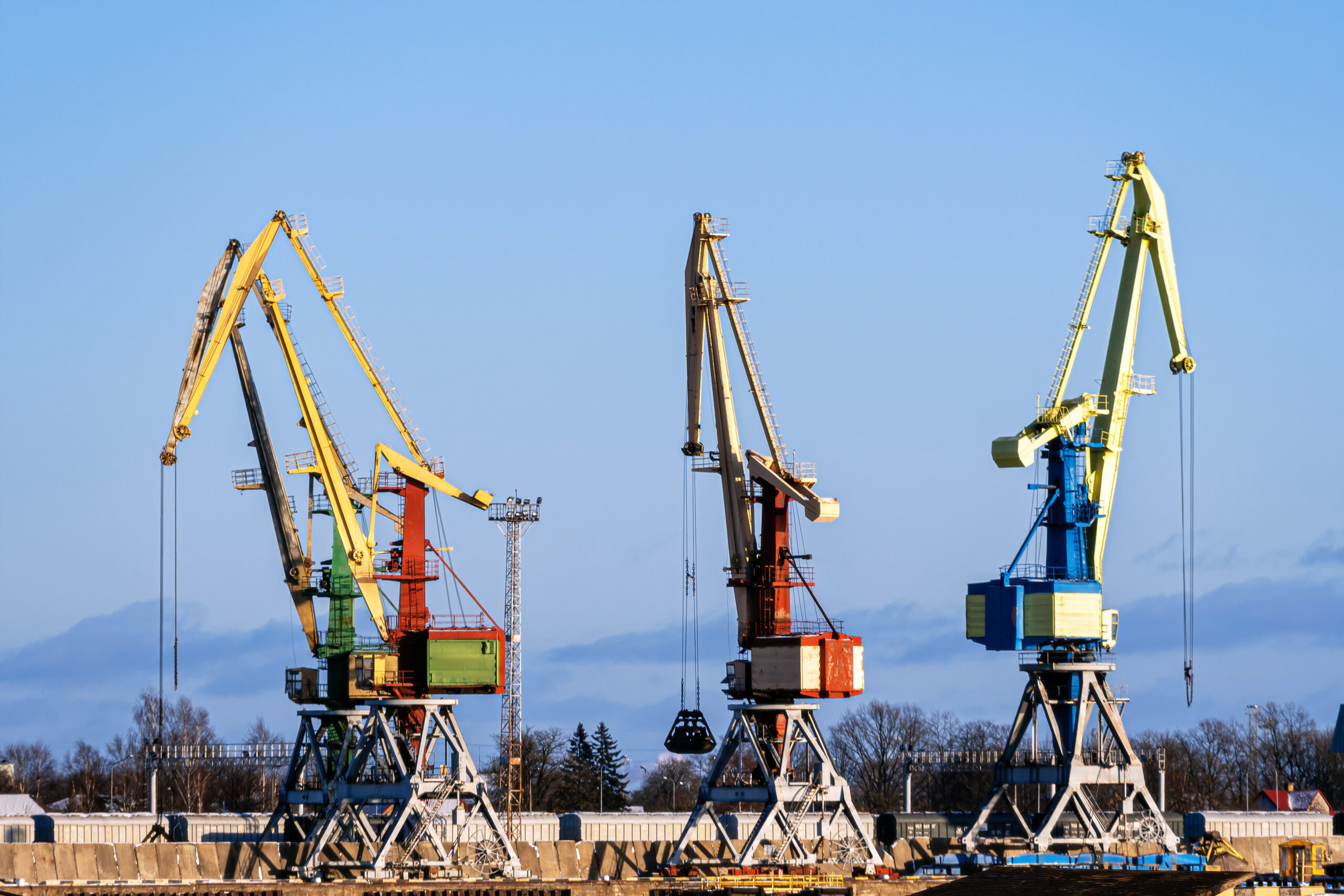 Heavy cranes engage in cargo handling at a bustling waterfront location on a sunny day.