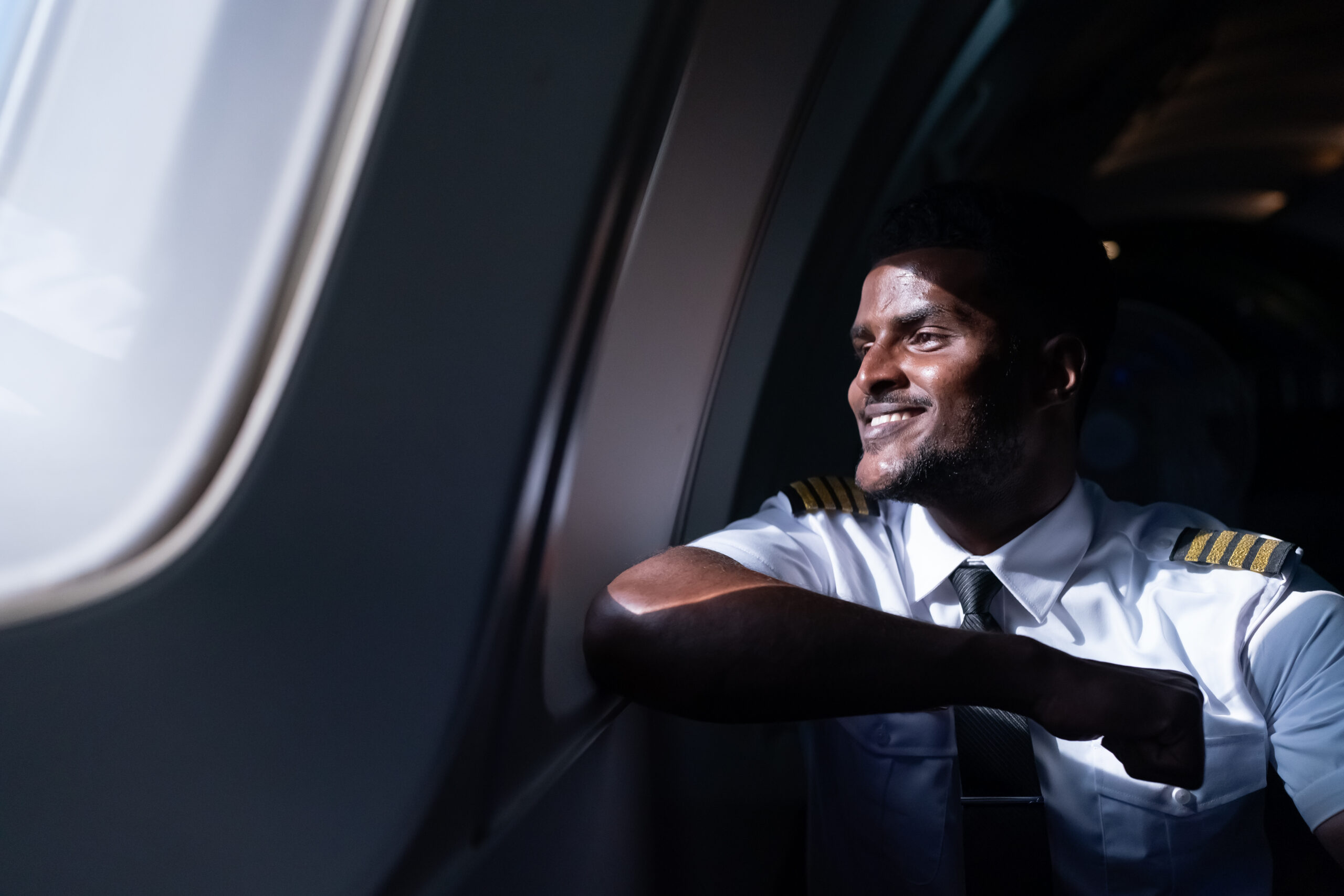 happy young pilot in professional uniform at airport. Male pilot sitting in airplane cockpit
