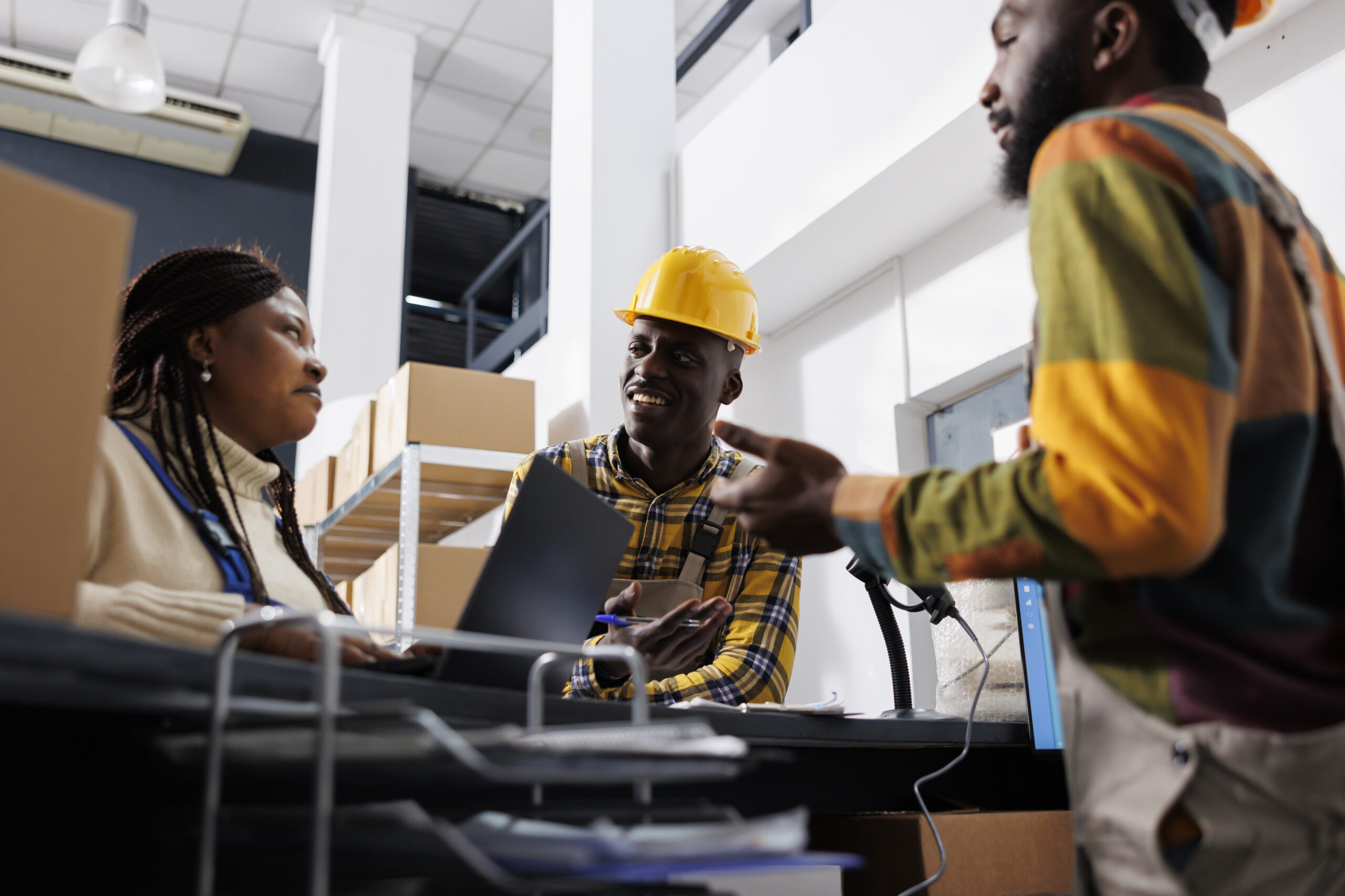 Storehouse workers explaining logistics manager parcels storing system, talking at reception desk. African american men and woman warehouse operators team discussing stock supply chain