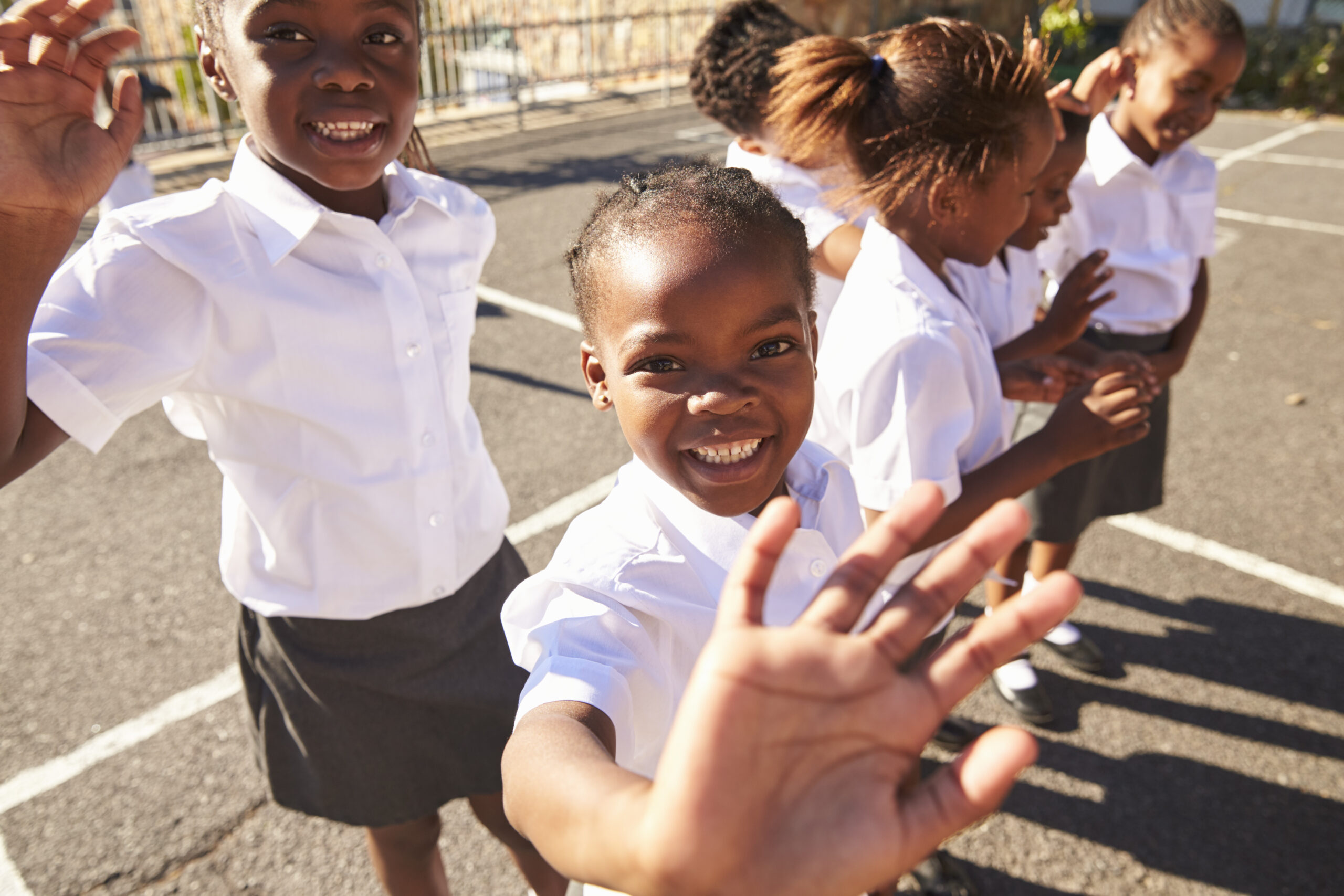 Young African schoolgirls in a playground waving to camera